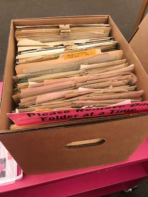 An archival box containing many, many slightly yellowed documents. A pink insert reads 'Please remove one folder at a time.' One file is labeled 'Patient Letters.'