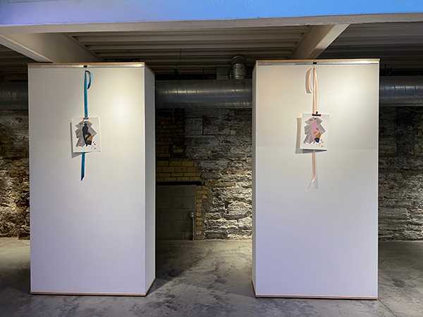 Image description: Two movable gallery walls painted with white paint hold two collages, each a variation of a similar collage. The collage is a figure against a backdrop created of found text outlining medication risks and interactions.